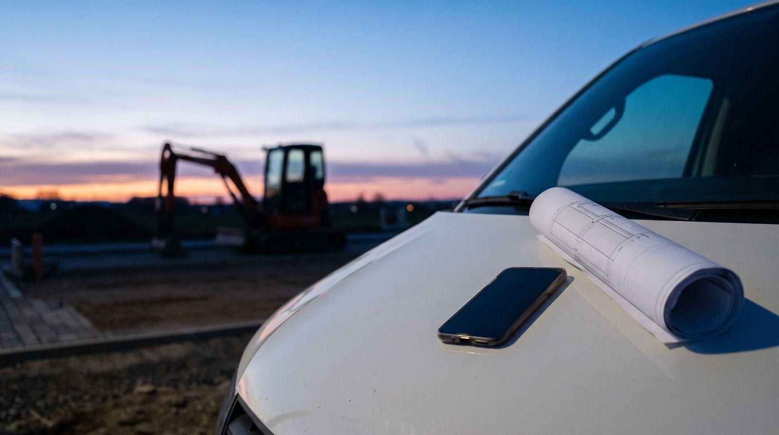 Fahrzeug mit geöffneter Heckklappe auf einer Baustelle in der Abenddämmerung, Werkzeugkisten und Bauplan sichtbar.